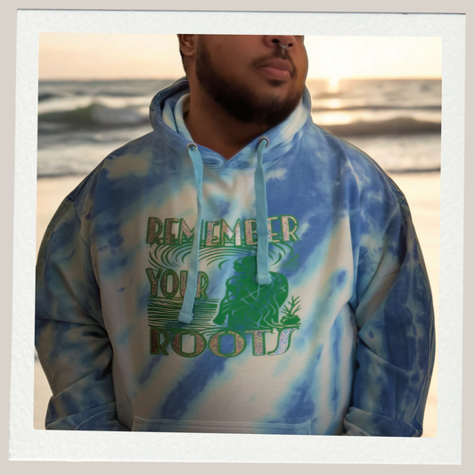 Person wearing a tie-dye hoodie with 'Remember Your Roots' text and graphic, standing on a beach.